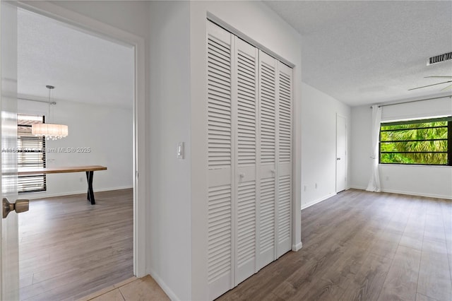 corridor featuring hardwood / wood-style flooring, a textured ceiling, and an inviting chandelier