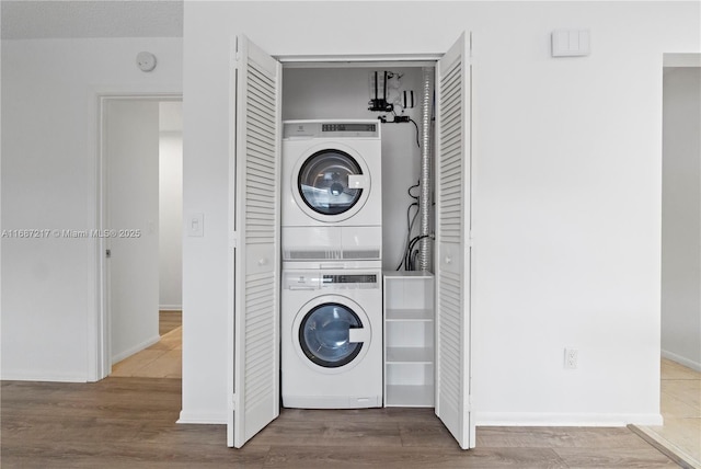 clothes washing area with hardwood / wood-style flooring and stacked washer and clothes dryer