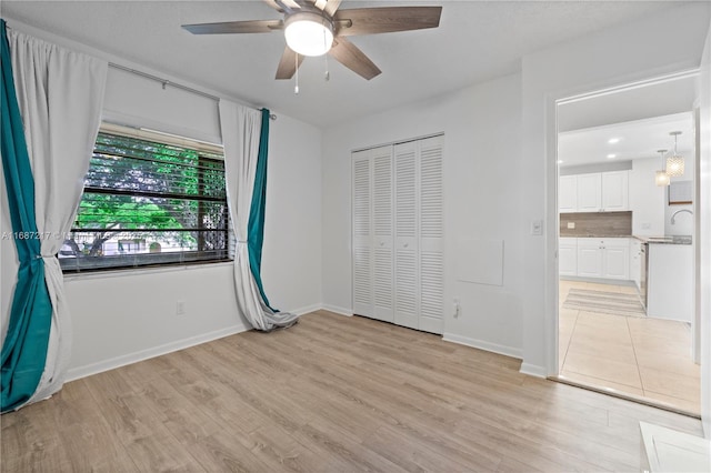 unfurnished bedroom with ceiling fan, a closet, sink, and light wood-type flooring