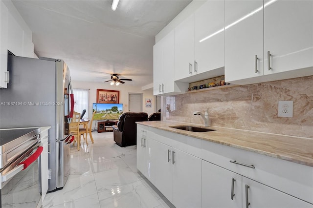 kitchen featuring tasteful backsplash, sink, stainless steel range oven, white cabinetry, and ceiling fan