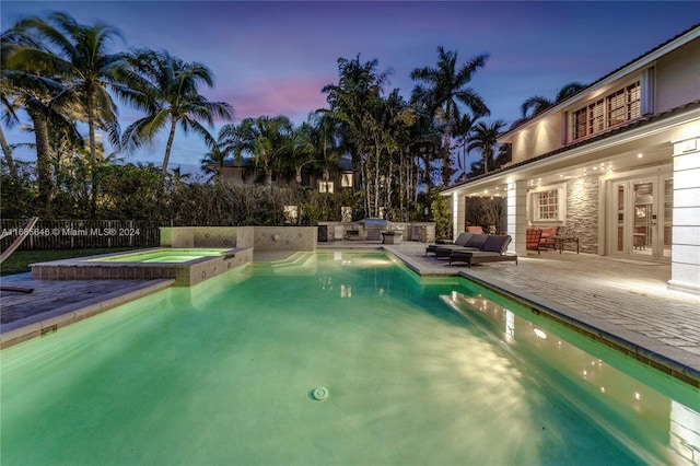 pool at dusk with an in ground hot tub, a patio, and french doors