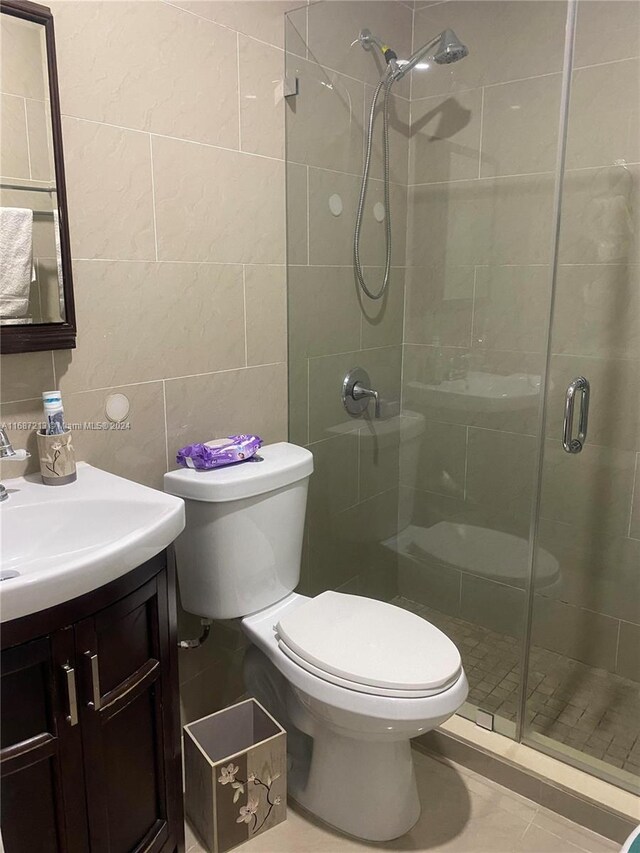 bathroom featuring tile patterned floors, toilet, vanity, tile walls, and an enclosed shower