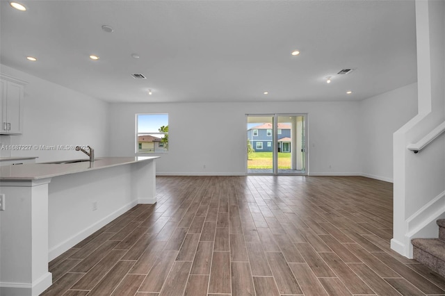 unfurnished living room featuring sink, dark wood-type flooring, and plenty of natural light