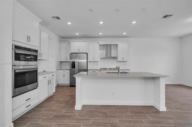 kitchen with white cabinetry, wall chimney range hood, stainless steel appliances, and an island with sink