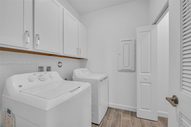 washroom with electric panel, washer and dryer, hardwood / wood-style flooring, and cabinets