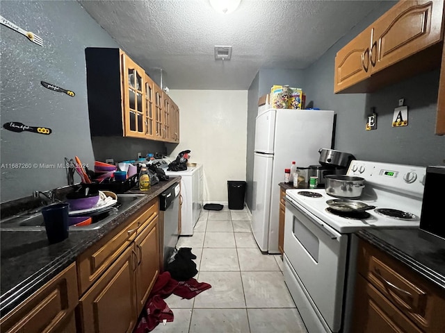 kitchen with washer / dryer, a textured ceiling, white appliances, and light tile patterned floors