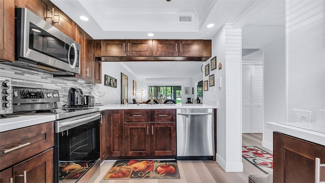 kitchen featuring decorative backsplash, appliances with stainless steel finishes, a tray ceiling, light hardwood / wood-style floors, and crown molding