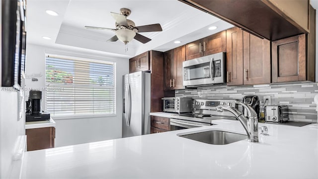 kitchen with decorative backsplash, stainless steel appliances, sink, a raised ceiling, and ceiling fan