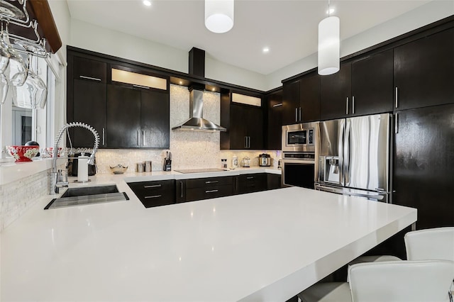 kitchen featuring tasteful backsplash, a breakfast bar, stainless steel appliances, wall chimney exhaust hood, and sink