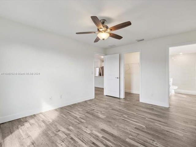 unfurnished bedroom featuring a spacious closet, a closet, hardwood / wood-style flooring, and ceiling fan