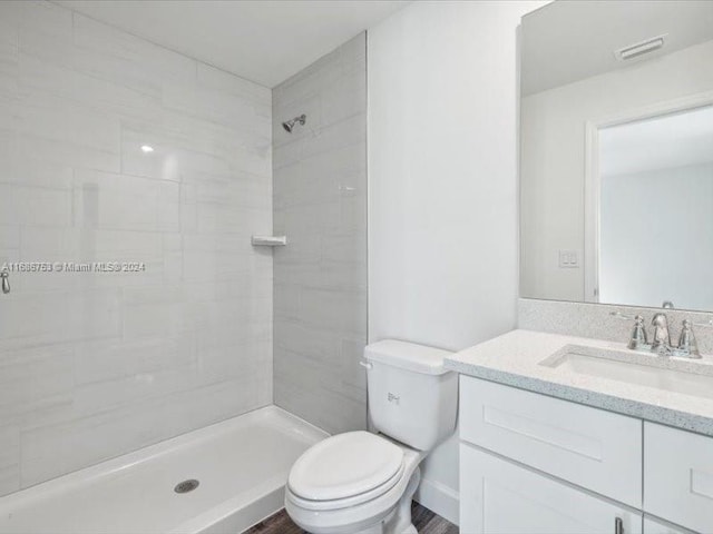 bathroom with vanity, toilet, wood-type flooring, and a tile shower