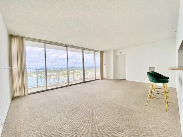 unfurnished living room with a textured ceiling, a water view, light colored carpet, and floor to ceiling windows