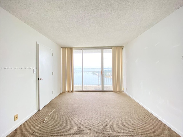 carpeted empty room with expansive windows, a textured ceiling, and a water view