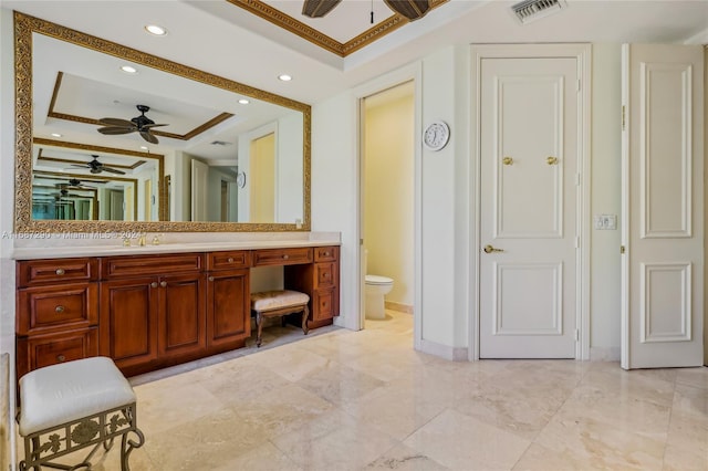 bathroom featuring a raised ceiling, toilet, ceiling fan, vanity, and crown molding