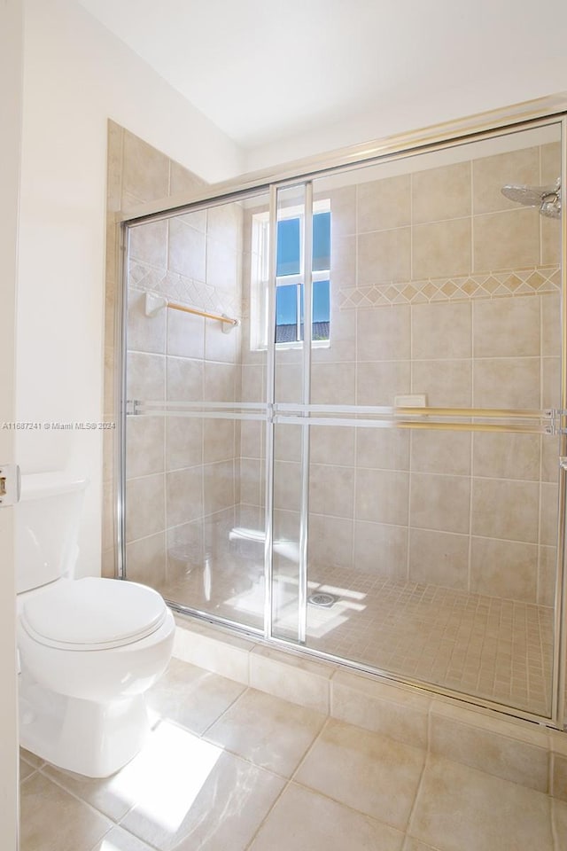 bathroom featuring toilet, a shower with shower door, and tile patterned flooring