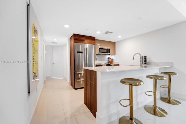 kitchen featuring kitchen peninsula, a kitchen breakfast bar, stainless steel appliances, sink, and light tile patterned flooring