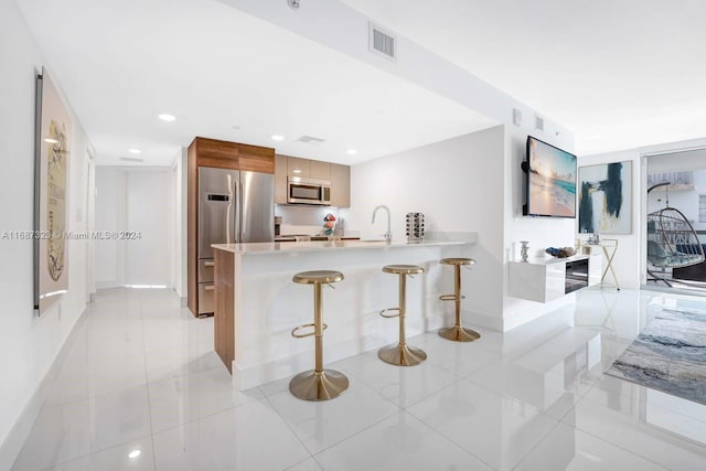 kitchen with light tile patterned flooring, a kitchen bar, kitchen peninsula, and stainless steel appliances