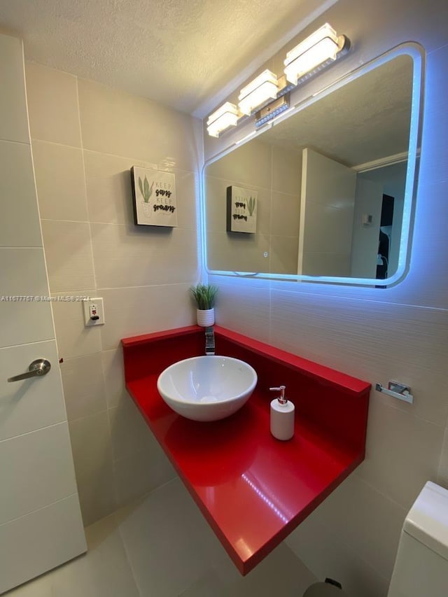 bathroom with toilet, a textured ceiling, tile walls, and sink