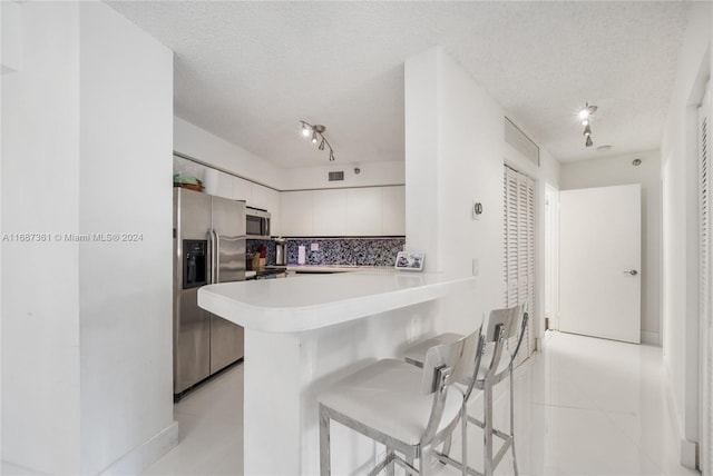 kitchen featuring a breakfast bar, appliances with stainless steel finishes, a textured ceiling, and white cabinets