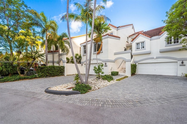 mediterranean / spanish house featuring a garage, a tiled roof, decorative driveway, and stucco siding