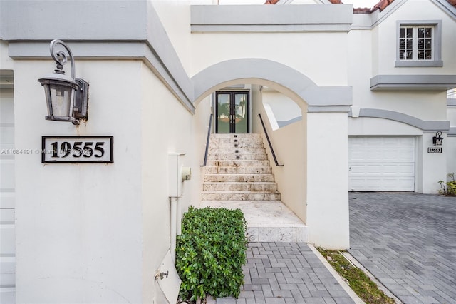 view of exterior entry with an attached garage, decorative driveway, and stucco siding