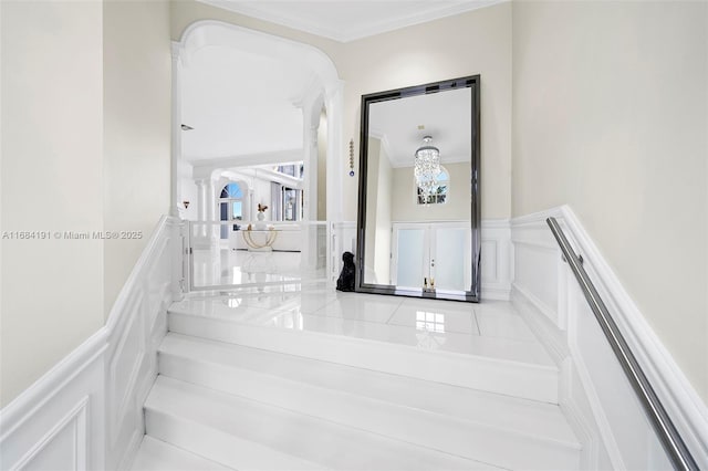 stairs featuring a wainscoted wall, ornate columns, a decorative wall, and crown molding