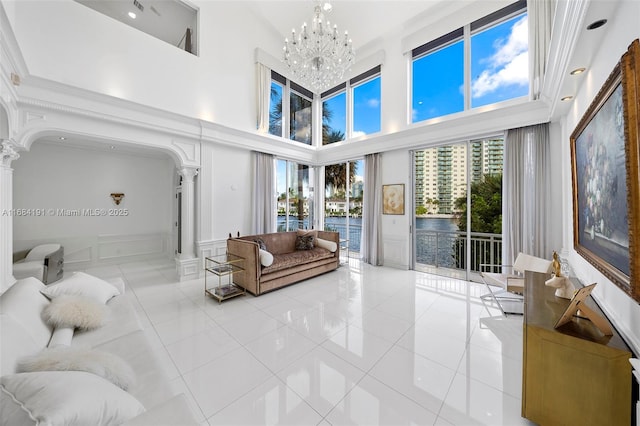 living area with a chandelier, a decorative wall, light tile patterned floors, and ornate columns