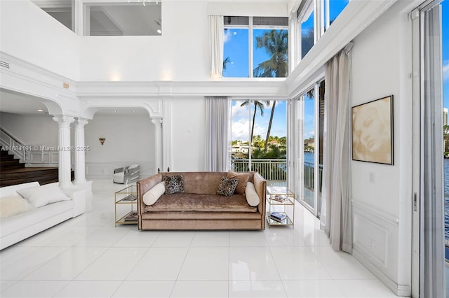 living area with a towering ceiling, light tile patterned floors, decorative columns, and arched walkways