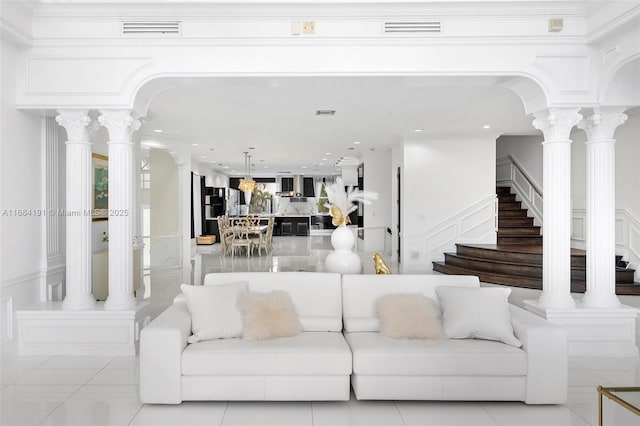 living area with arched walkways, light tile patterned floors, visible vents, stairs, and ornate columns