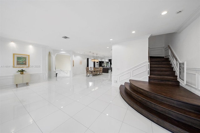 hall featuring arched walkways, crown molding, visible vents, a decorative wall, and stairs