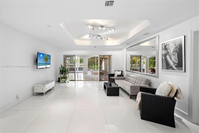 living area featuring light tile patterned floors, visible vents, a raised ceiling, and a wealth of natural light