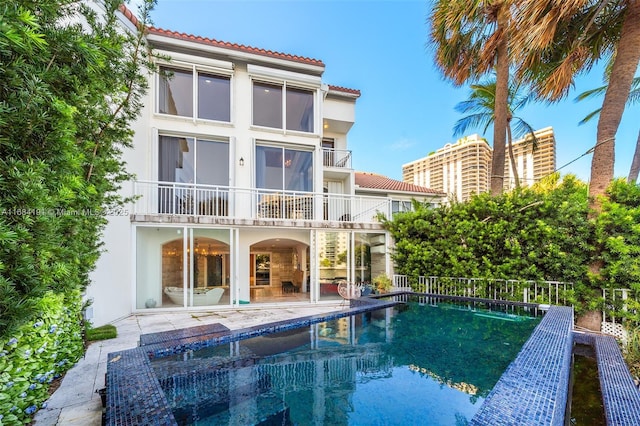 back of house featuring a balcony, a tile roof, a fenced in pool, and stucco siding