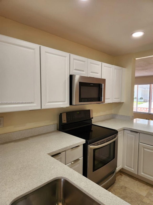 kitchen featuring appliances with stainless steel finishes, white cabinets, and light stone counters