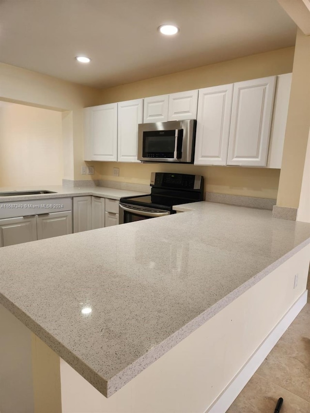 kitchen with light stone countertops, white cabinetry, kitchen peninsula, and stainless steel appliances