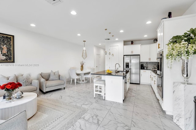 kitchen with dark countertops, a breakfast bar, appliances with stainless steel finishes, marble finish floor, and a sink