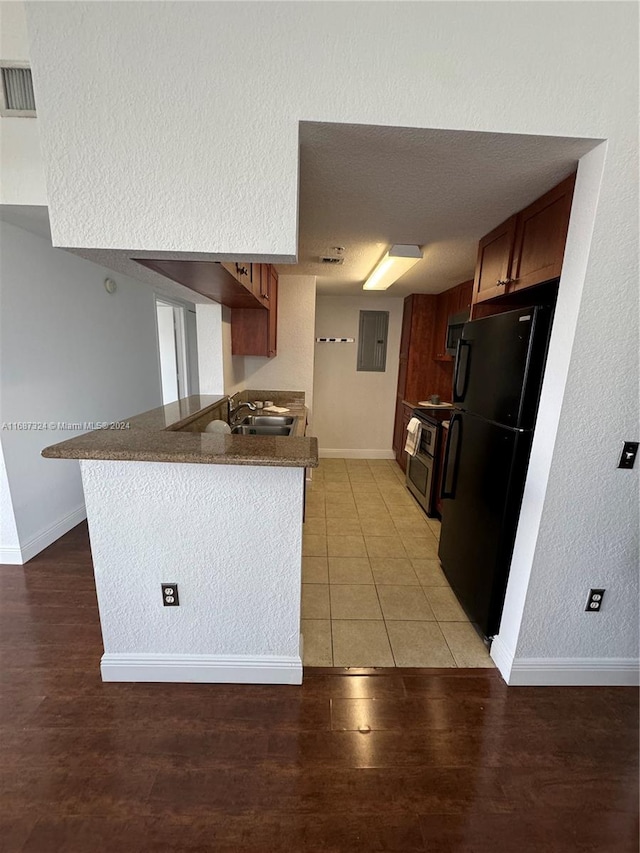 kitchen featuring kitchen peninsula, stainless steel range with electric cooktop, light hardwood / wood-style flooring, black refrigerator, and sink