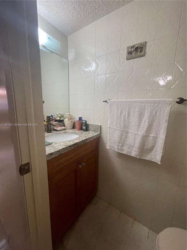 bathroom featuring vanity, toilet, tile walls, and a textured ceiling