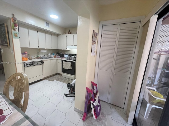 kitchen featuring white dishwasher, white cabinetry, light tile patterned floors, and range