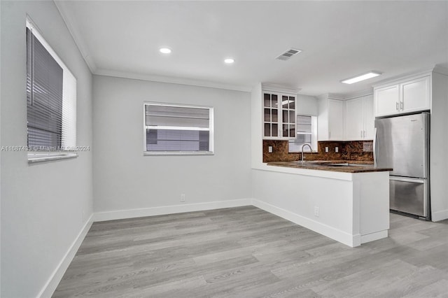 kitchen with light hardwood / wood-style flooring, kitchen peninsula, stainless steel fridge, white cabinets, and ornamental molding