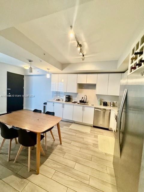 kitchen with track lighting, appliances with stainless steel finishes, white cabinetry, light hardwood / wood-style flooring, and sink