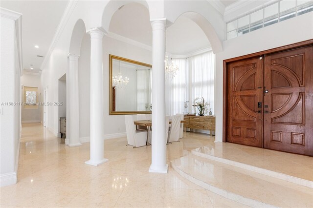 foyer entrance with decorative columns, baseboards, and crown molding