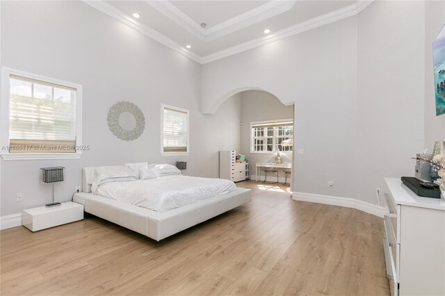 bedroom featuring arched walkways, a towering ceiling, baseboards, ornamental molding, and light wood finished floors