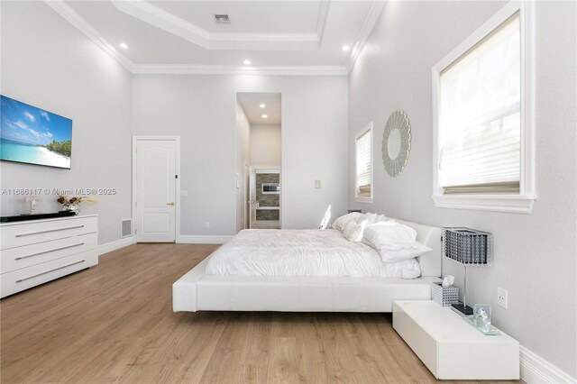 bedroom with crown molding, a tray ceiling, visible vents, and light wood-style floors