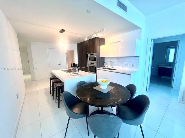 kitchen featuring stainless steel double oven, dark brown cabinetry, light tile patterned floors, white cabinets, and a kitchen island with sink