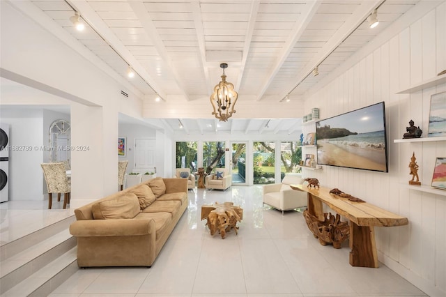 tiled living room with beamed ceiling, stacked washing maching and dryer, track lighting, and a notable chandelier