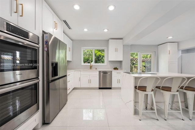 kitchen featuring light tile patterned flooring, a breakfast bar, sink, stainless steel appliances, and white cabinets