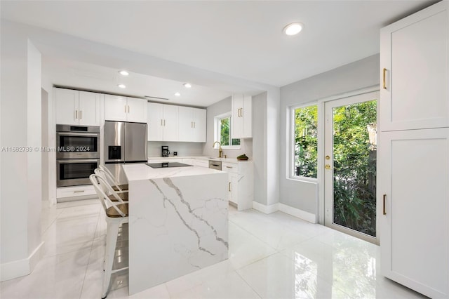 kitchen featuring appliances with stainless steel finishes, a breakfast bar, white cabinetry, a center island, and light stone countertops