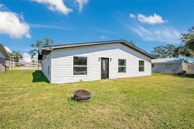 back of house with an outdoor fire pit and a lawn