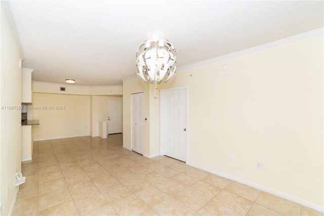 tiled empty room featuring ornamental molding, a textured ceiling, and a chandelier