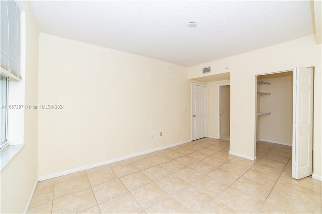 unfurnished bedroom with a closet, a textured ceiling, a spacious closet, and light tile patterned floors